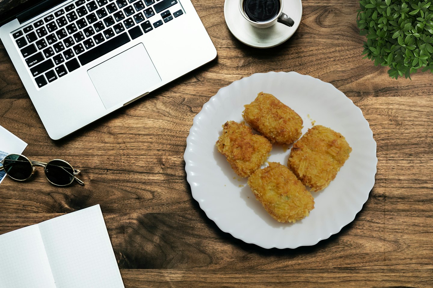 Laptop, Kaffee und Kroketten auf einem Holztisch.