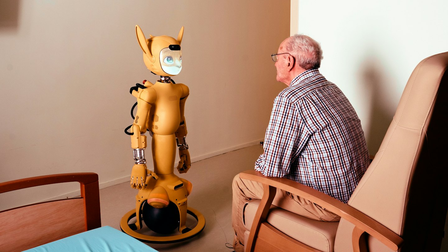 Ein älterer Mann betrachtet einen freundlichen Roboter in einem Raum.